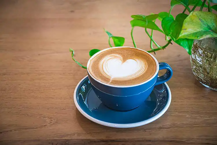 Schön eine blaue tasse heißen cappuccino-kaffee mit latte art auf einem hölzernen couchtisch, selektiver fokus für getränkehintergrund