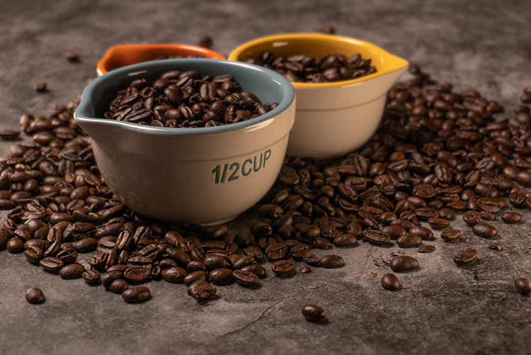 Frische rohe bio-kaffeebohnen in vielen bunten messbechern mit unterschiedlichen größen