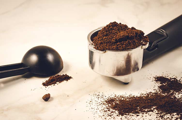 Halter gefüllt mit gemahlenem kaffee ein schwarzer löffel/halter gefüllt mit gemahlenem kaffee ein schwarzer löffel auf einem marmorhintergrund. selektiver fokus