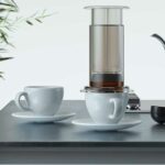 Frisch zubereiteter schwarzer kaffee in einer kaffeemaschine in der nähe von weißen kaffeetassen in einer hellen, modernen küche. alternative möglichkeiten der kaffeezubereitung. 3d-rendering