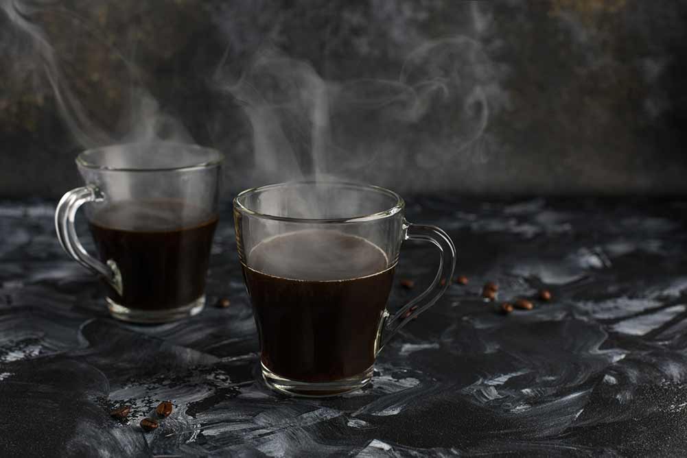 Zwei glasbecher schwarzer kaffee. dunkler hintergrund mit kaffeebohnen