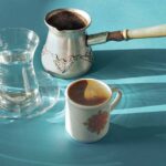 Kaffee im osten. eine kleine tasse kaffee, ein jezwa und ein türkisches glas sauberes wasser auf einer blauen oberfläche. hartes licht. horizontale ausrichtung.