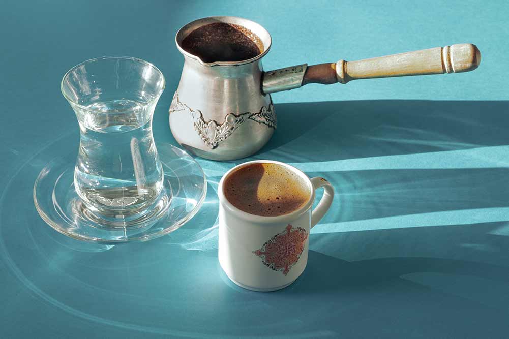 Kaffee im osten. eine kleine tasse kaffee, ein jezwa und ein türkisches glas sauberes wasser auf einer blauen oberfläche. hartes licht. horizontale ausrichtung.