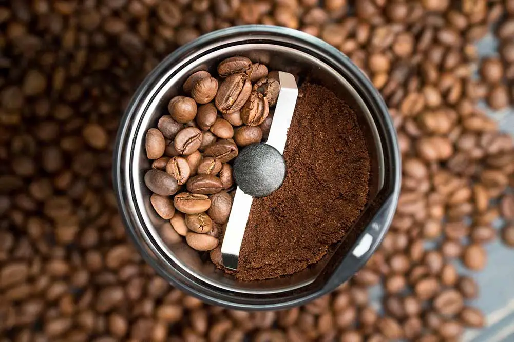Kaffeemühle mit kaffeebohnen isoliert. in der einen hälfte der kaffeemühle befinden sich ganze kaffeekörner und in der anderen hälfte gemahlener kaffee