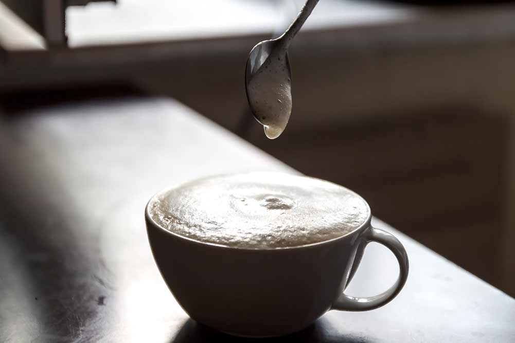 Tasse kaffee mit schaum, der von einer menschlichen hand gerührt wird.