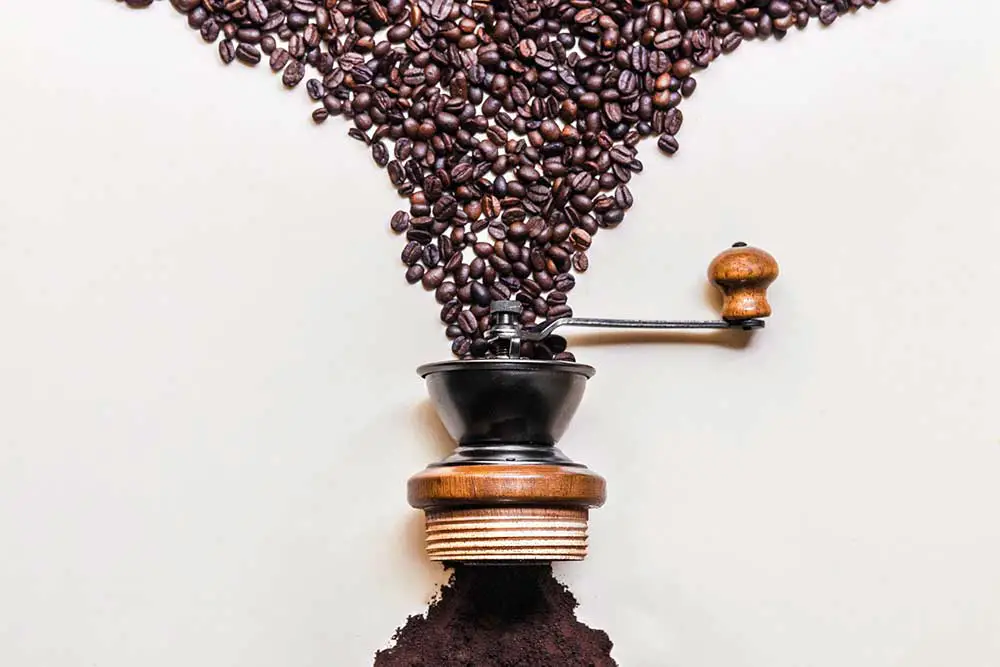 Geröstete schwarze kaffeebohnen, die in eine retro-holzmühle fallen, und gemahlener kaffee in der bildmitte herauskommen, der auf weißem hintergrund kopiert wird, platz für kommerzielle designarbeiten