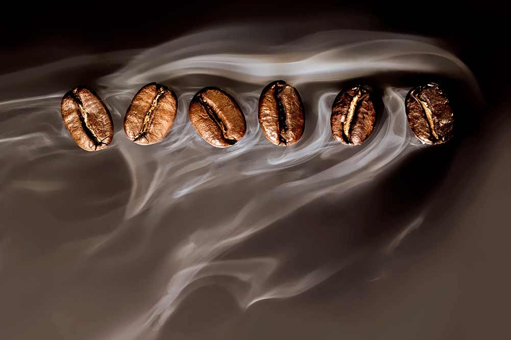 Geröstete kaffeebohnen. samen von frisch geröstetem kaffee mit rauch. kaffeebohnen-nahaufnahme mit betonung auf dem korn mit rauch.