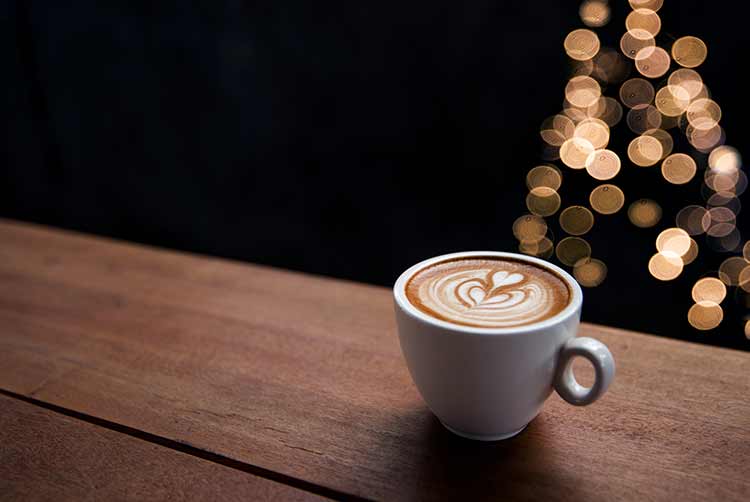 Leckerer cappuccino mit einigen verschwommenen lichtern vom weihnachtsbaum.