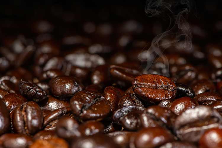 Dunkelbraune geröstete kaffeebohnen mit rauch unter künstlichem licht für den hintergrund