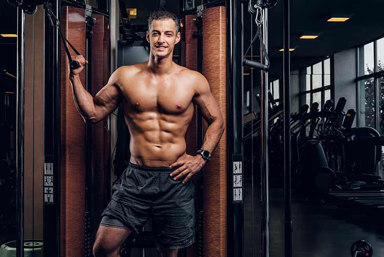 Glücklicher lächelnder mann macht übungen mit trainingsgeräten im dunklen fitnessstudio.