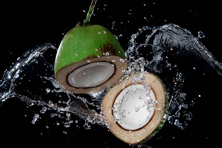 Gebrochene kokosnuss mit spritzwasser oder explosion, die in der luft einzeln auf schwarzem hintergrund fliegt