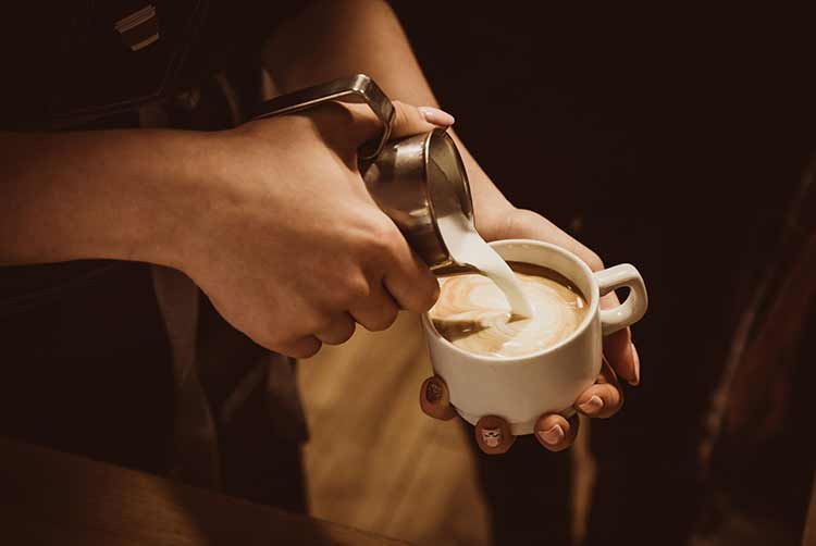 Barista macht aromatisierten cappuccino, gießt milch in kaffee
