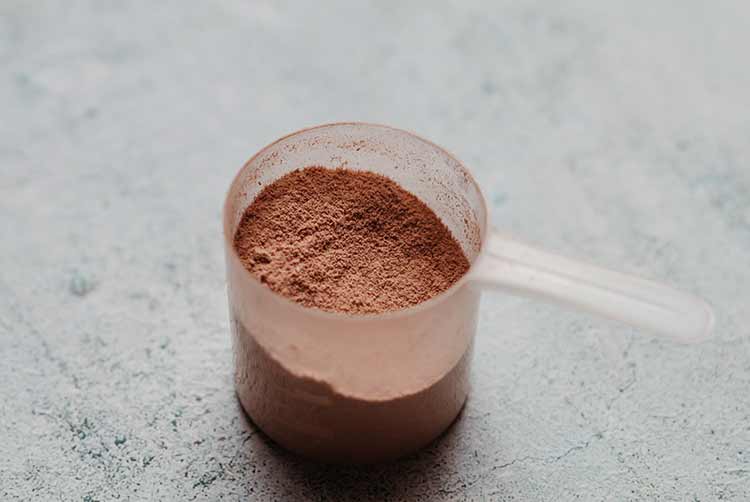 Schaufel oder löffel whey protein mit sichtbarer textur. schokoladengeschmack. konkreter hintergrund