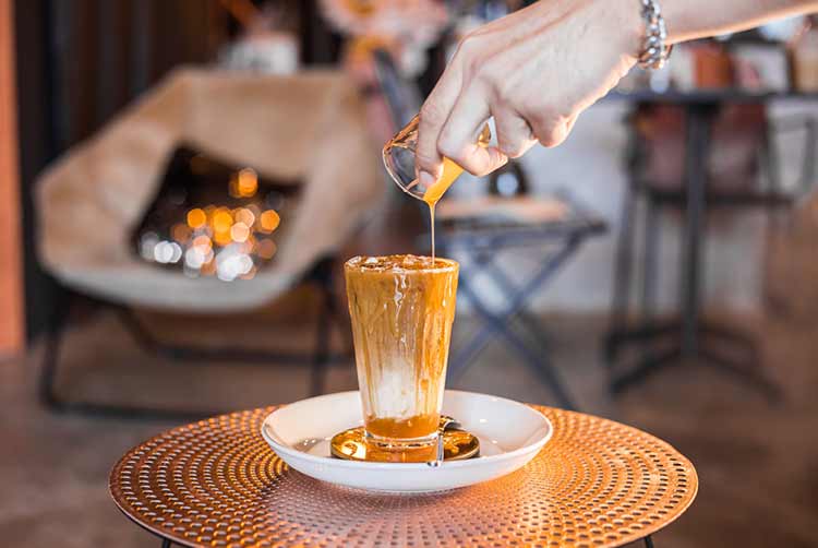 Eiskaffee mit milch in hohen gläsern auf dem tisch mit karamellsirup darüber gegossen.