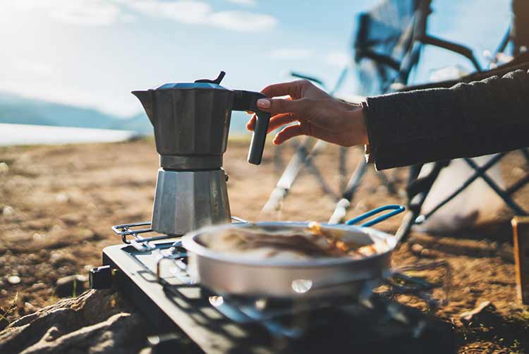 Moka kaffeekanne im freien, picknick am morgen auf dem campingplatz, person, die heißes getränk auf dem naturcampingplatz kocht, kocher bereitet frühstück zu, tourismuserholung draußen