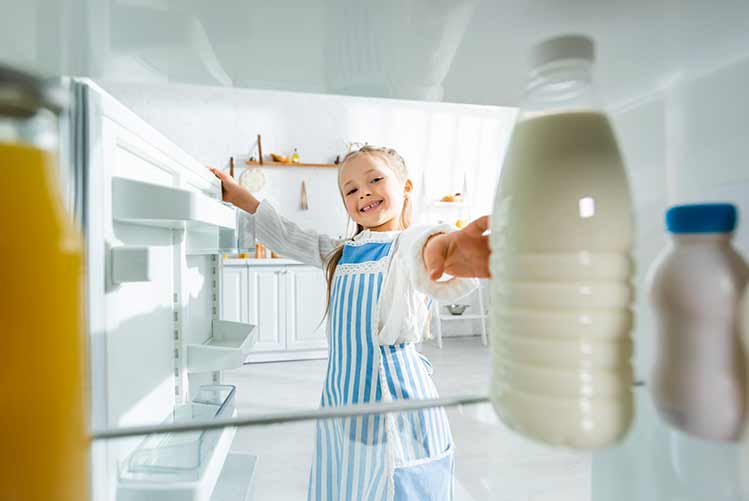Selektiver fokus des lächelnden kindes, das eine flasche mit milch aus dem kühlschrank nimmt