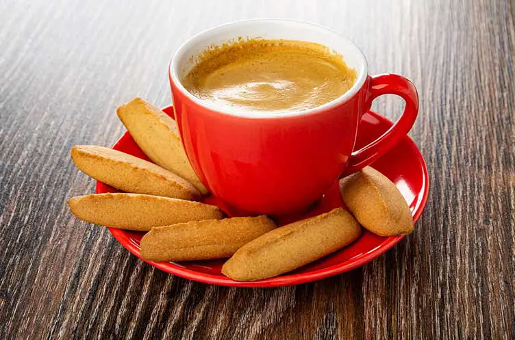 Kaffee-espresso in tasse, ein paar kekse auf roter untertasse auf dunklem holztisch