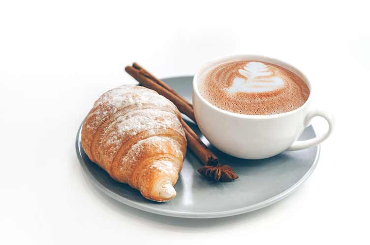 Frisch gebackenes croissant mit kaffeetasse und latte art, zimt und sternanis. isoliert