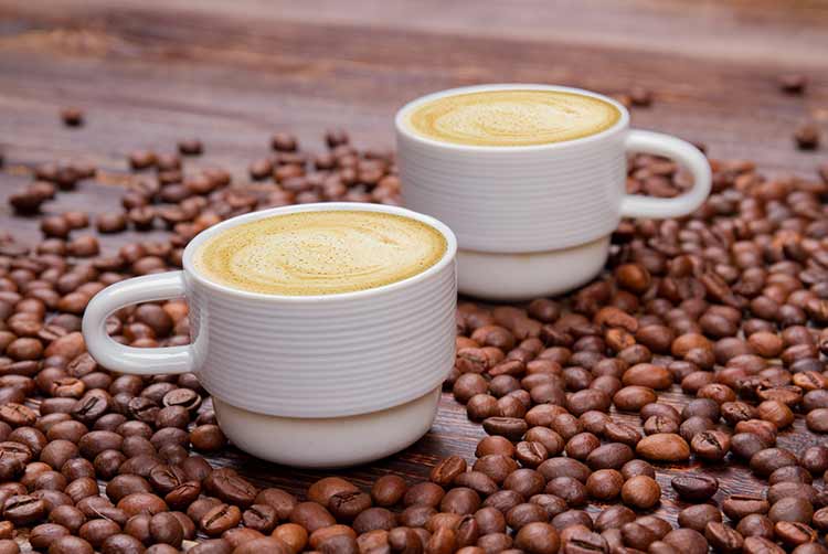 Zwei tassen kaffeebohnen mit milchigem schaum. haufen gerösteter kaffeebohnen hautnah.