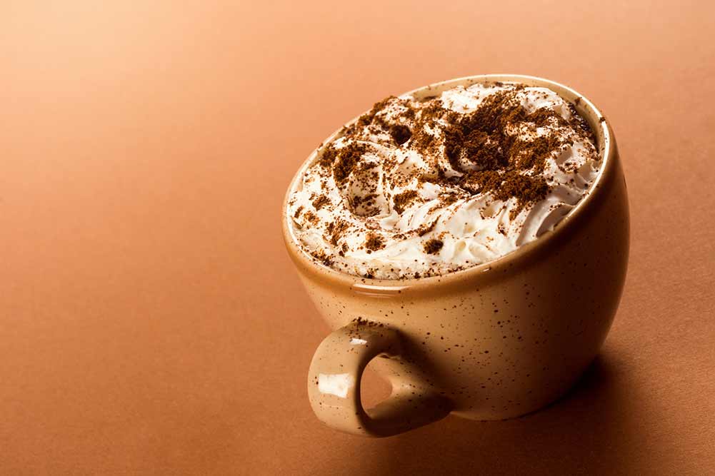 Tasse cappuccino mit schlagsahne und kaffeepulver auf beigem hintergrund.
