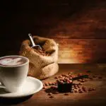 Eine tasse latte art mit gerösteten kaffeebohnen im beutel