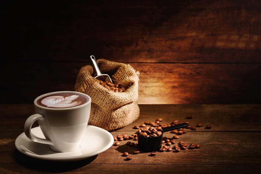 Eine tasse latte art mit gerösteten kaffeebohnen im beutel