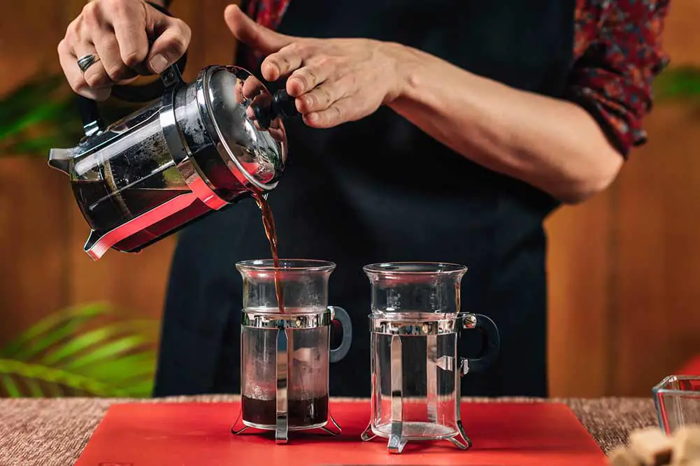 Französischer presskaffee. hände einer barista, die kaffee aus der französischen presse in eine kaffeetasse aus glas gießt