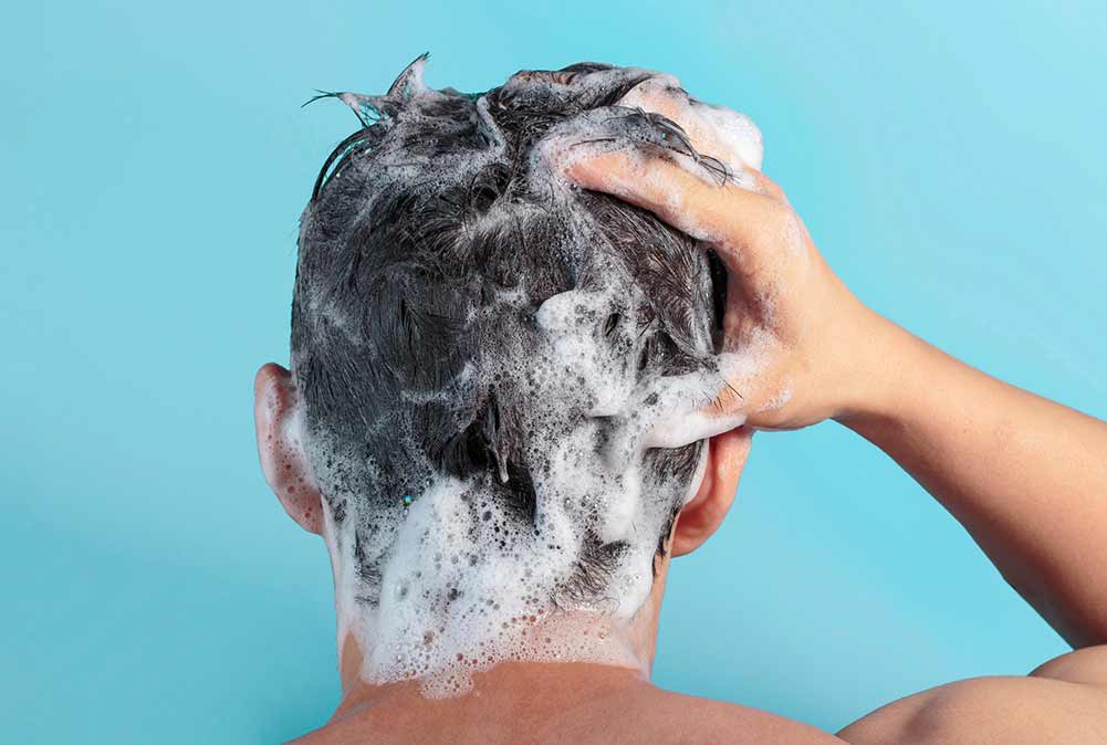 Männliche hand wäscht seinen kopf mit shampoo und schaum auf blauem hintergrund, rückansicht