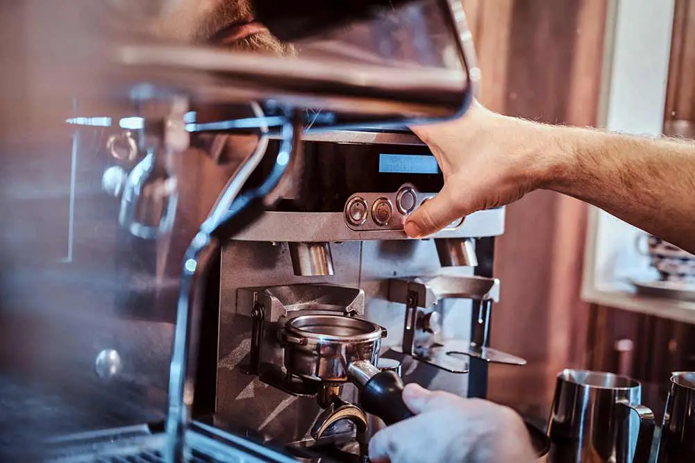 Nahaufnahme eines baristas, der einen siebträger mit schwarzem gemahlenem kaffee hält und an einer kaffeemaschine in einem café oder restaurant arbeitet