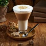 Café latte macchiato geschichteter kaffee in einer glastasse. die tasse steht auf einem rustikalen holztisch.