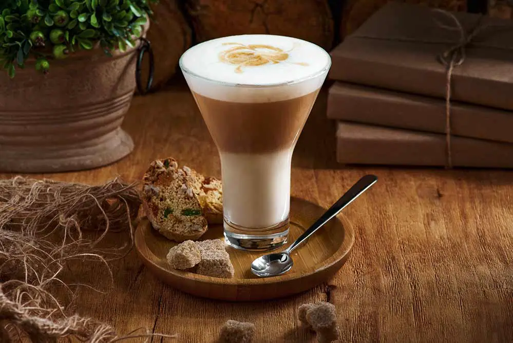 Café latte macchiato geschichteter kaffee in einer glastasse. die tasse steht auf einem rustikalen holztisch.