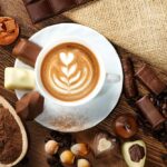 Tasse leckeren kaffee mit schokolade und haselnüssen, die mit sackleinen auf hölzernem hintergrund bedeckt sind