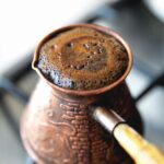 Alte kaffeemaschine türke auf öfen kaffee, schaum kochender kaffee, frühmorgens nahaufnahme