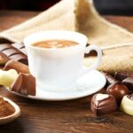 Tasse leckeren kaffee mit schokolade und haselnüssen, die mit sackleinen auf hölzernem hintergrund bedeckt sind