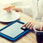 Schnellimbiss-, leute-, technologie- und diätkonzept - nah oben von der frau mit tabletten-pc-computer, von pizza und von kolabaum, die bei tisch kalorien zählen