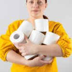 Frauenhand hält weiche toilettenpapierrollen auf grauem hintergrund mit kopienraum. komposition für werbung, artikel oder banner