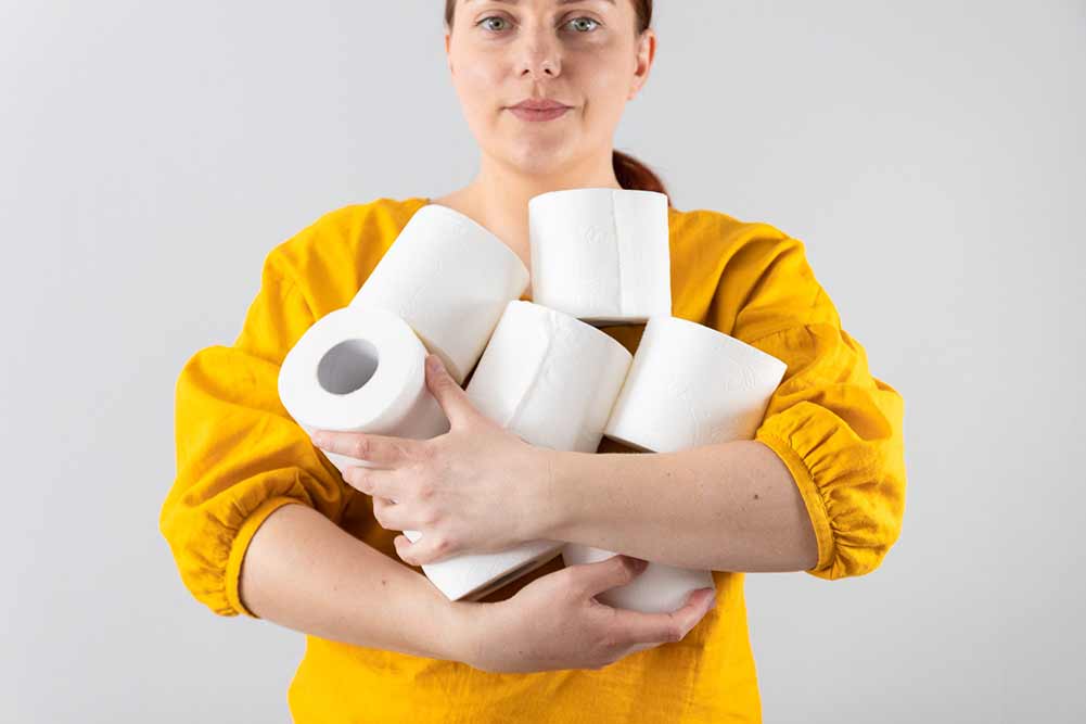 Frauenhand hält weiche toilettenpapierrollen auf grauem hintergrund mit kopienraum. komposition für werbung, artikel oder banner