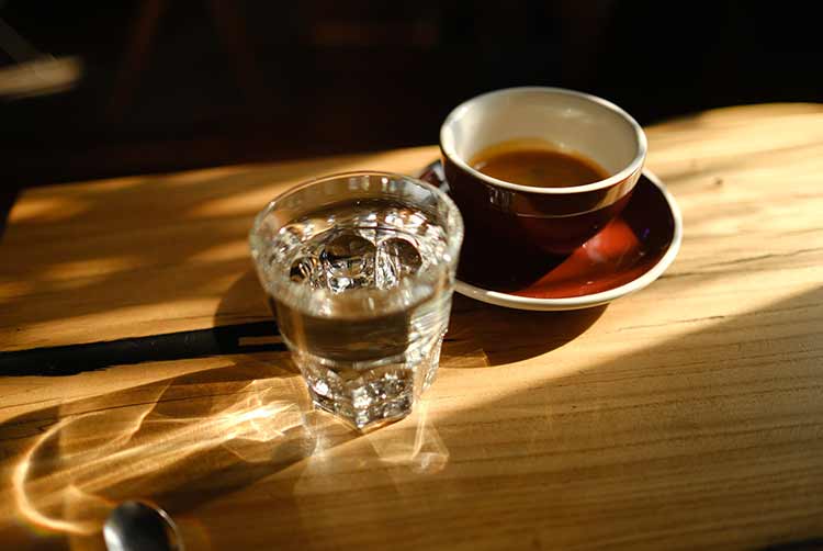 Schwarzer kaffee in einer tasse und einem transparenten glas mit wasser auf einem hölzernen hintergrund. blendung in der sonne. schönes licht