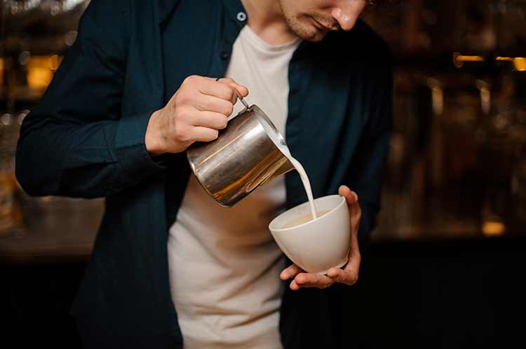 Brunet barkeeper gießt eine milch in die weiße tasse tasse kaffee auf der theke