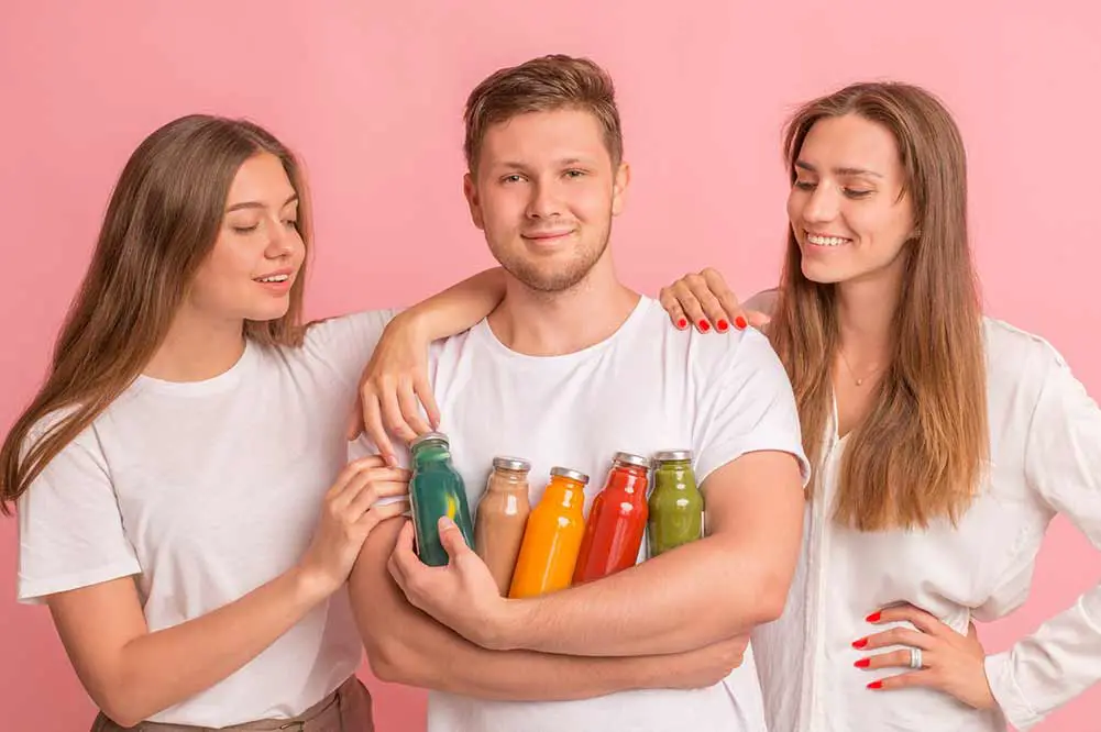 Teenager-unternehmen, das gesunde getränke für die party zubereitet, mädchen, die jungen mit detox-komplex anschauen, rosafarbener hintergrund