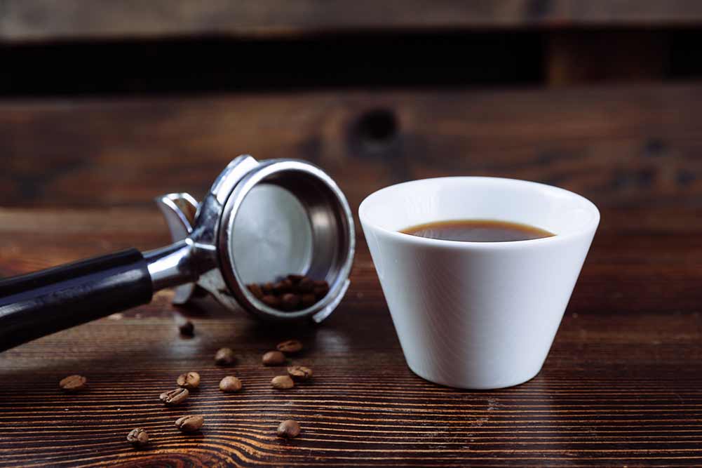 Eine tasse schwarzen kaffee, geröstete kaffeebohnen und ein espressomaschinenhalter auf dunklem hintergrund.