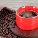 Kaffee serviert in einer tasse mit kaffeebohnen auf der seite auf tischplatte