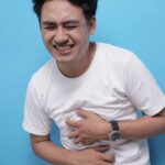 Porträt eines jungen asiatischen mannes, der seinen magen zusammendrückt, weil er bauchschmerzen hat