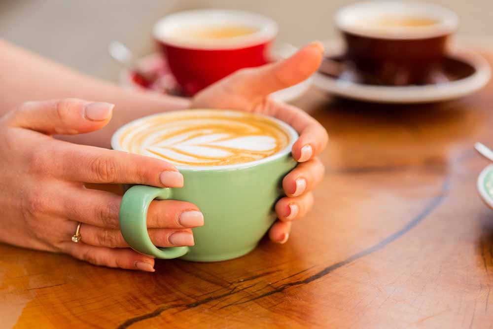Tasse kaffee mit herzform. guten morgen kaffee. barista serviert kaffee. morgenstimmung im café. herz latte art. frau hält heiße tasse kaffee mit herzform. latte art auf holztisch