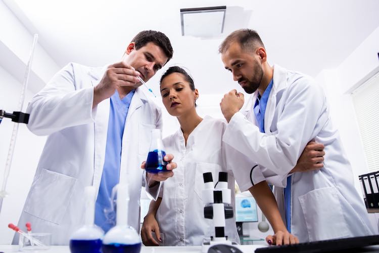 Team von wissenschaftlern im weißen kittel, die eine probe einer rauchenden blauen flüssigkeit betrachten