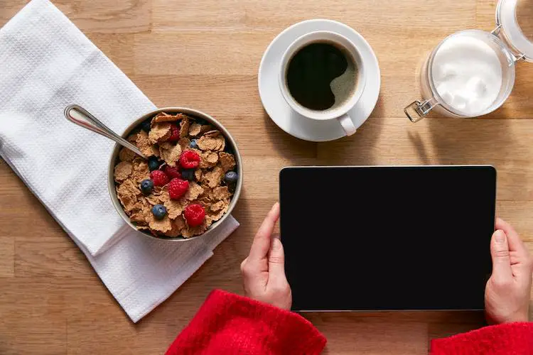 Obenliegende flache lage der frau mit digitalem tablet auf dem tisch zum frühstück mit müsli und kaffee