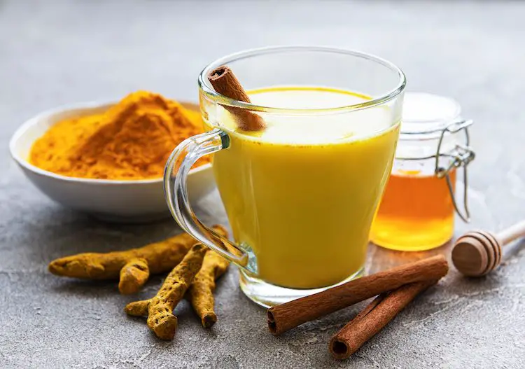 Gelbes kurkuma-latte-getränk. goldene milch mit zimt, kurkuma, ingwer und honig auf grauem betonhintergrund.