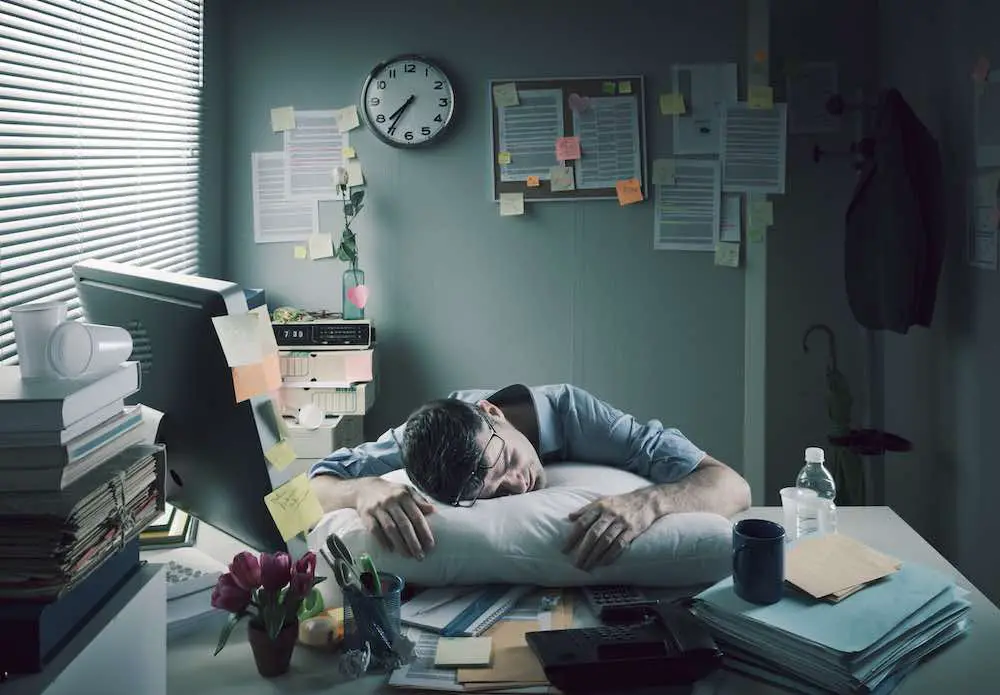 Erschöpfter geschäftsmann schläft am arbeitsplatz mit einem kissen auf seinem schreibtisch.