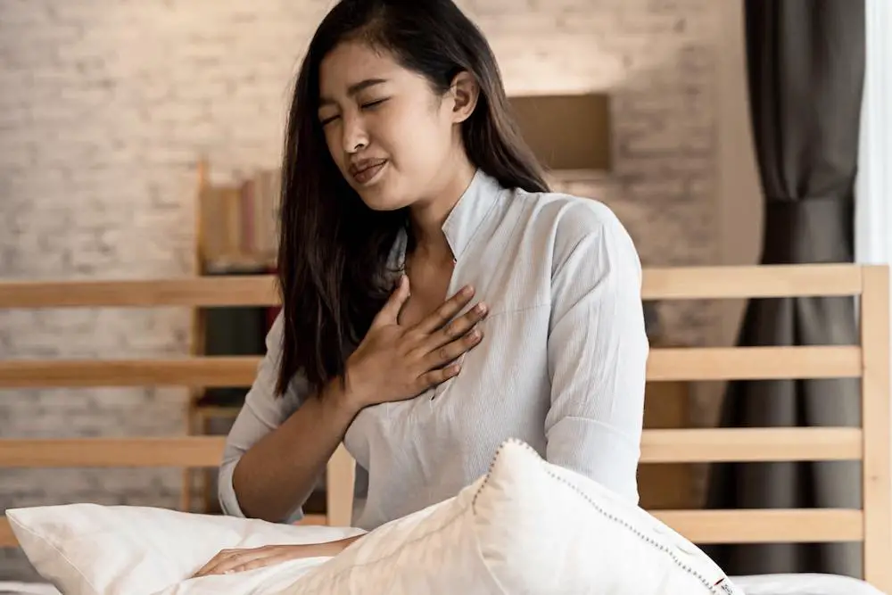 Porträt einer jungen asiatischen frau aus den 20er jahren, die nachts im schlafzimmer schwierigkeiten beim atmen hat. kurzatmigkeit, asthma, probleme beim atmen. coronavirus-symptome.