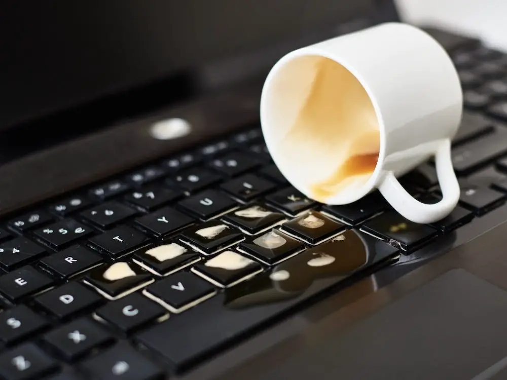 Verschütten sie kaffee aus einer weißen tasse auf der computer-laptop-tastatur. schäden am computer durch verschüttete flüssigkeit